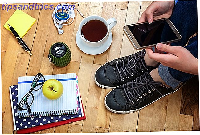 Person med smartphone, kop kaffe, notesbog osv.